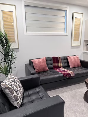 Uma sala de estar moderna com um sofá de couro preto, um vaso de planta e quadros na parede.