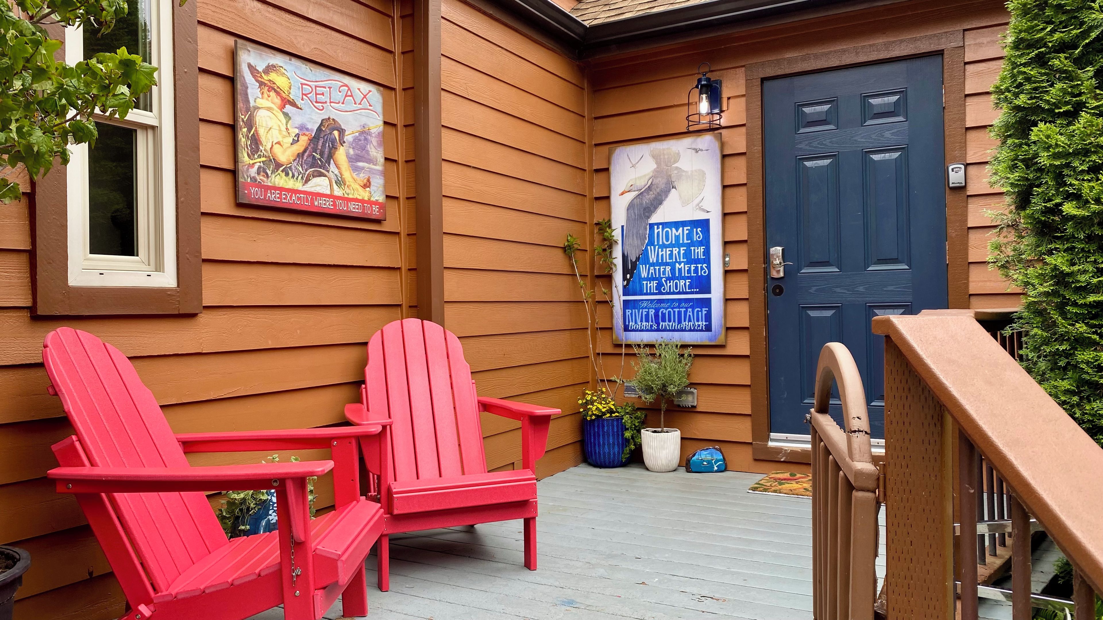 Een houten huisje met een blauwe deur, twee rode Adirondack-stoelen en twee posters aan de muur.