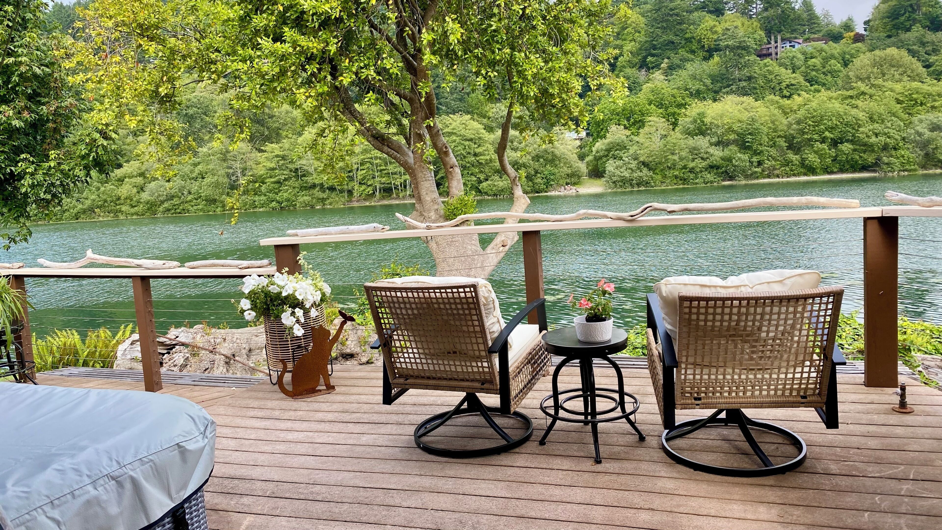 Eine Terrasse mit Korbmöbeln und einem Tisch, mit Blick auf einen See und Bäume im Hintergrund.