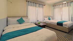 Quarto de hotel com duas camas, uma mesa de cabeceira e uma janela com cortinas.