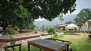 Mesa e bancos de madeira numa área ao ar livre com grama, com vista para uma montanha ao fundo.