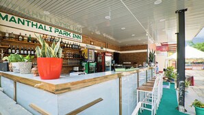 Uma área de bar com balcão de recepção, diversos tipos de bebidas e uma grande planta em vaso.
