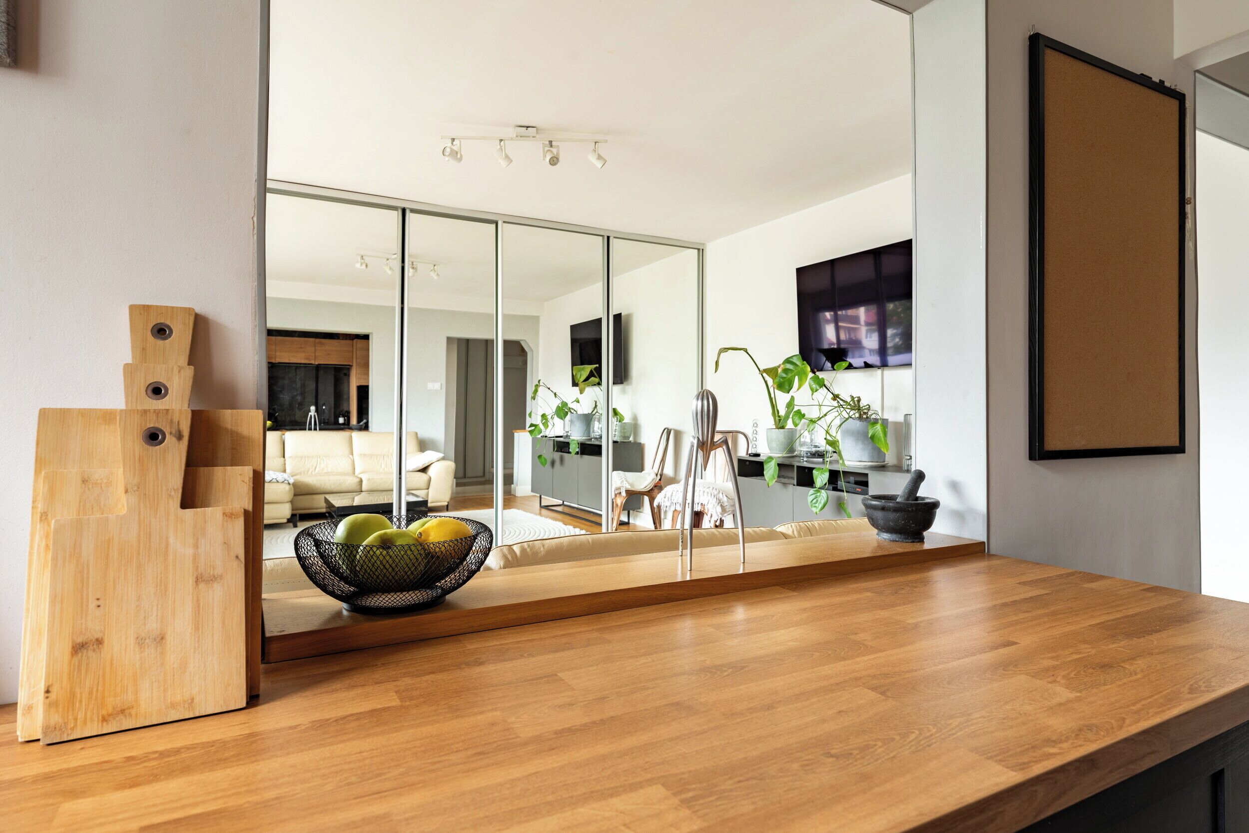 A modern kitchen with a wooden countertop, a fruit bowl, and a large mirror reflecting the room.