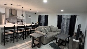 Een moderne keuken met witte kasten, een eethoek met tafel en stoelen, en een zithoek met een bank en salontafel.