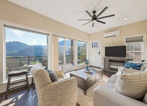 Un ampio soggiorno con una grande TV, posti a sedere confortevoli, un caminetto e un balcone con vista sulle montagne.