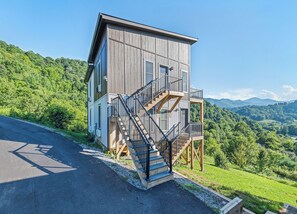 Edificio a due piani con facciata in legno, una scala e vista su una rigogliosa valle verde.