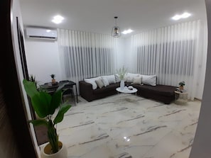 A modern living room with a sectional sofa, a coffee table, and a potted plant. - Cozy 1-bedroom apartment in serene Amman with AC (Amman)