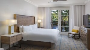 Una camera d'albergo con un letto grande, televisione, una sedia e un balcone con tende.