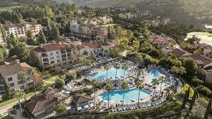 Vista aerea di un resort con diversi edifici, una piscina centrale con lettini e vegetazione circostante.