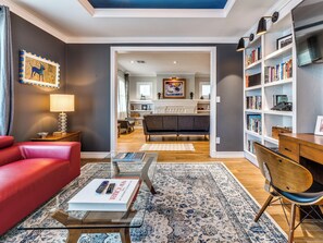 A modern living room with a red sofa, a glass coffee table, a bookshelf, and a dining area with a wooden table and chairs. - Quiet Luxury Oasis in Uptown OKC (Oklahoma City)