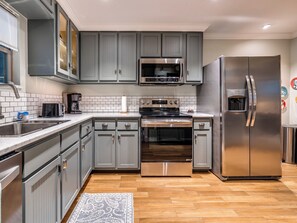 A modern kitchen with grey cabinets, stainless steel appliances, and a wooden floor. - Quiet Luxury Oasis in Uptown OKC (Oklahoma City)
