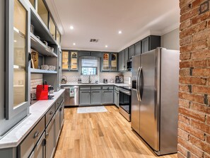 A modern kitchen with grey cabinets, a stainless steel refrigerator, and a wooden floor. - Quiet Luxury Oasis in Uptown OKC (Oklahoma City)