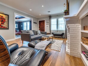 Een moderne woonkamer met een bank, lederen fauteuils, een salontafel en een open haard.