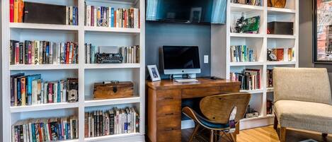 A study room with a wooden desk, a computer, a chair, and bookshelves filled with books.