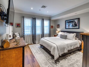 Ein Schlafzimmer mit einem Bett, Nachttischen, einem Schreibtisch mit Computer und einem Fenster mit Vorhängen.