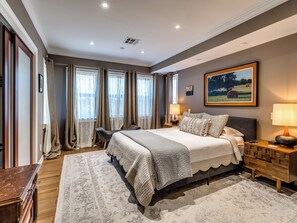 A bedroom with a large bed, bedside tables, a nightstand, a painting on the wall, and a window with curtains. - Quiet Luxury Oasis in Uptown OKC (Oklahoma City)
