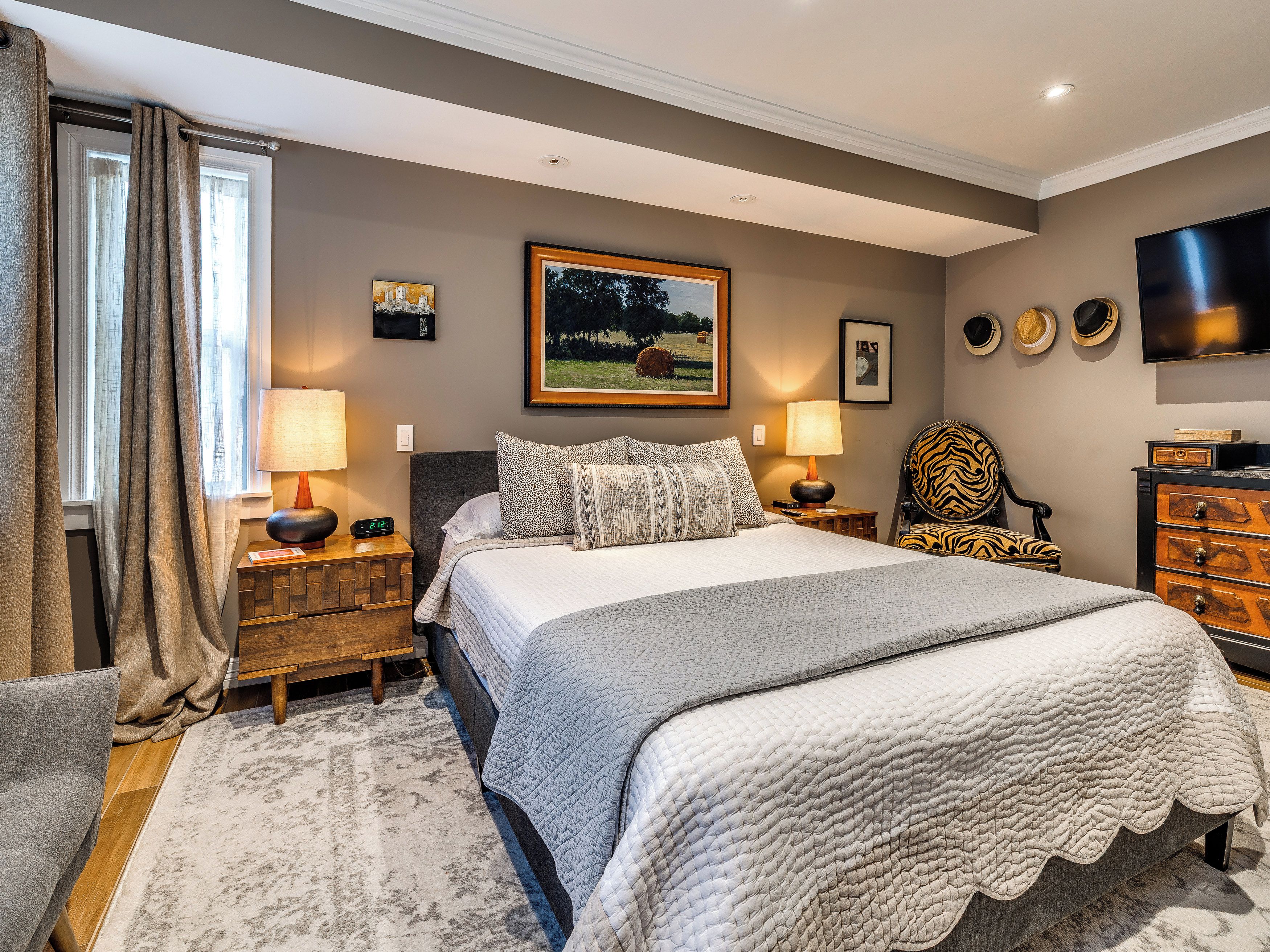 A bedroom with a bed, two bedside tables, a chair, a TV, and artwork on the wall.