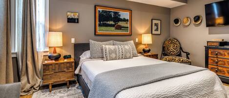 A bedroom with a bed, two bedside tables, a chair, a TV, and artwork on the wall.