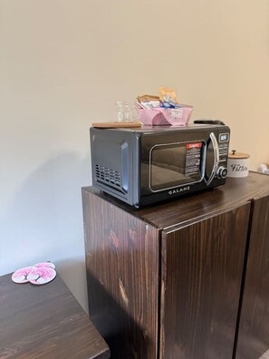 A microwave on a wooden cabinet with a pink packet and a glass pitcher on top.