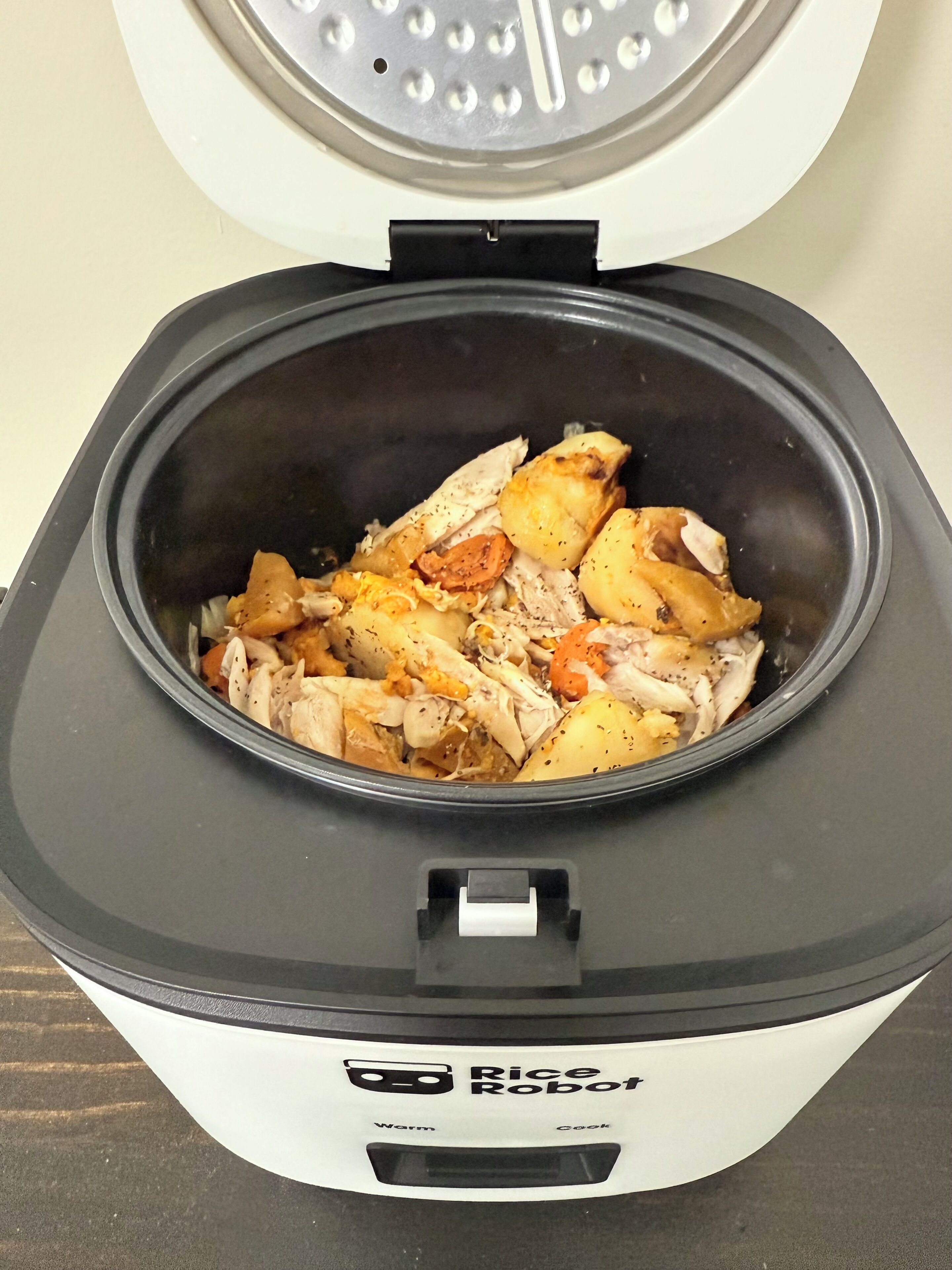 A rice cooker with a lid open, containing cooked chicken and potatoes.