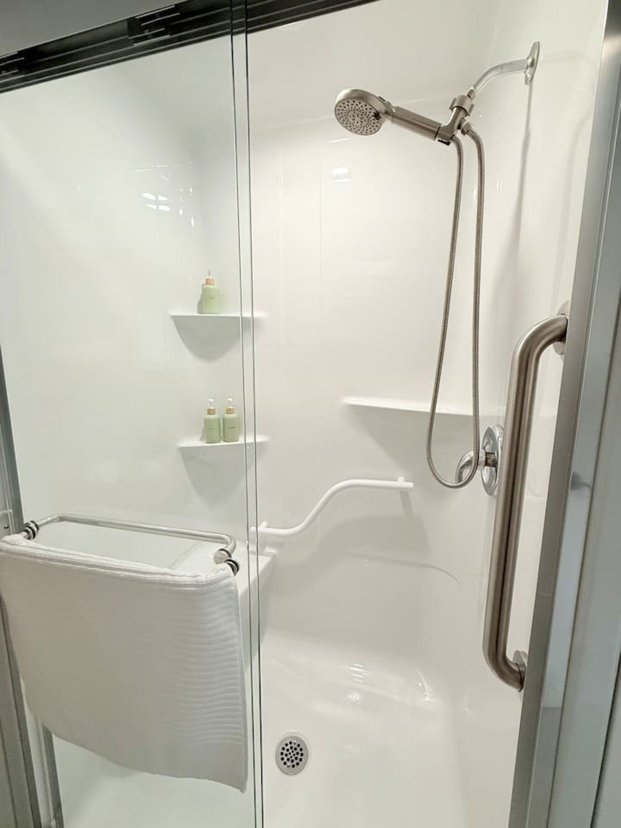 Une cabine de douche fermée par des parois en verre, dotée d’un pommeau de douche à main, d’un porte-serviettes et d’une étagère pour les articles de toilette.