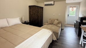 Un dormitorio con una cama grande, un armario de madera, un equipo de aire acondicionado y un escritorio pequeño con una silla.