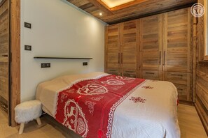 A bedroom with a bed, a small stool, wooden wardrobe, and a shelf. - CHALET LE 1244 - CHAMPAGNY EN VANOISE (CHAMPAGNY EN VANOISE)