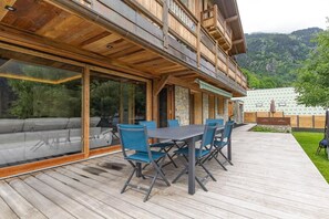 Eine Holzterrasse mit Esstisch und Stühlen, einer Sitzecke und Blick auf eine gebirgige Landschaft.