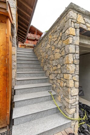 Eine Steintreppe führt zu einer Holztür, im Hintergrund ist ein Gebäude zu sehen.