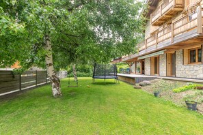 Ein Garten mit Schaukel, Trampolin und einem Steinhaus mit Holzbalkonen.