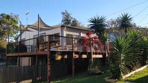 Una casa de dos plantas con balcón, rodeada por una valla de madera, y un letrero que indica alquiler vacacional.
