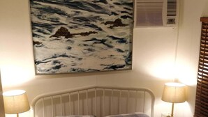 Un dormitorio con colcha a cuadros, dos lámparas de noche, un aire acondicionado de pared y un cuadro con una escena marina.