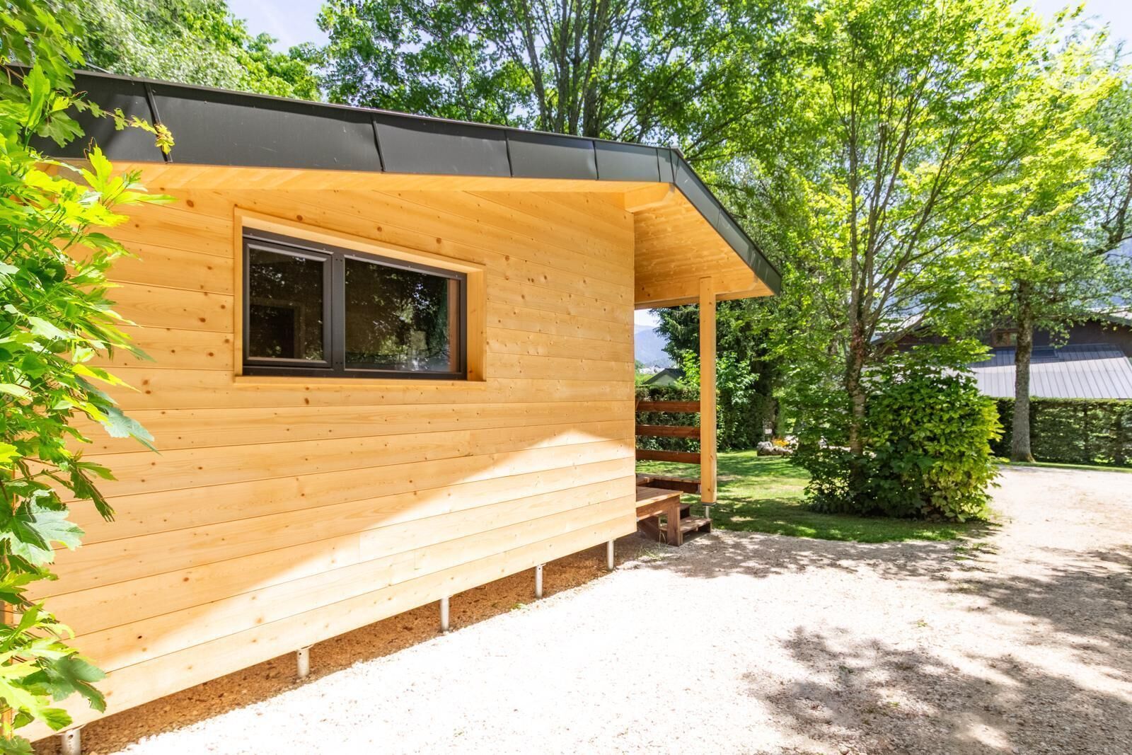 A wooden cabin with a window, a porch, and a gravel driveway.