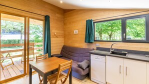A compact room with a wooden interior, a dining table with chairs, a sofa, a window with curtains, and a built-in sink. - Chalet du Sud - LE CHATELARD (LE CHATELARD)