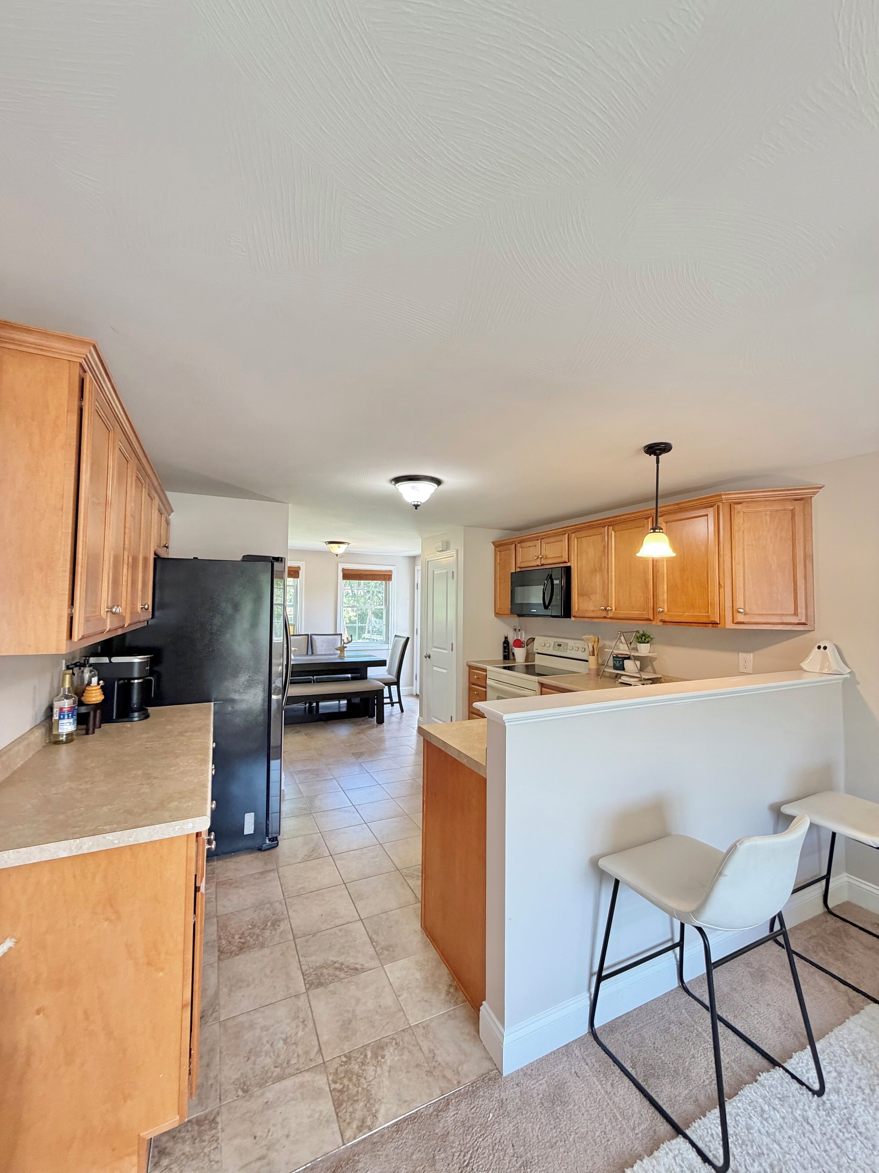 A kitchen with wooden cabinets, a black refrigerator, a microwave, and a dining area with a table and chairs.