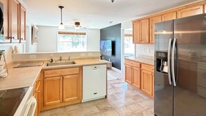 A modern kitchen with wooden cabinets, a stainless steel refrigerator, a dishwasher, and a large island with a sink.