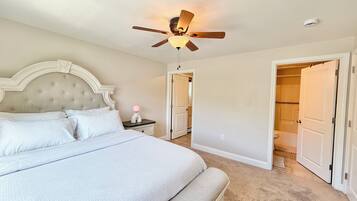 A bedroom with a bed, a nightstand, a ceiling fan, and a door leading to a bathroom.