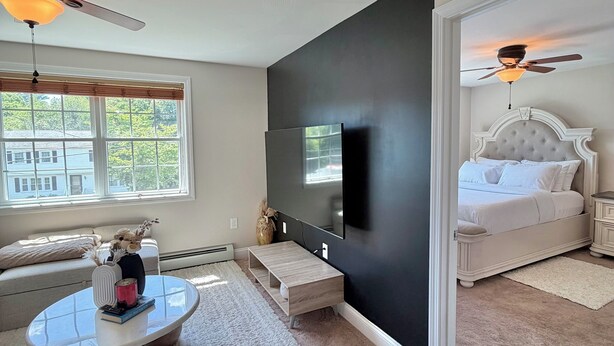 A modern bedroom with a bed, a TV, a ceiling fan, and a window with blinds.
