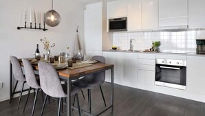 A modern kitchen with white cabinets, a built-in oven, and a dining area with a wooden table and grey chairs. - 5 Star Holiday Home in Uddevalla (Uddevalla)