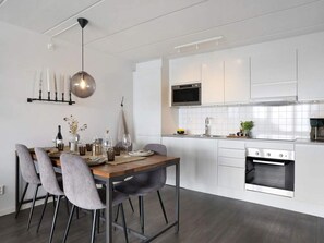 Eine moderne Küche mit weißen Schränken, einem eingebauten Backofen und einem Essbereich mit Holztisch und grauen Stühlen.
