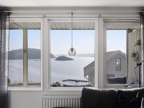 Ein Zimmer mit großem Fenster und Blick auf ein Gewässer, einem Heizkörper und einem grauen Sofa.