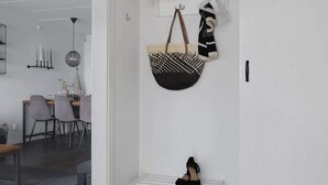 A white bench with black shoes, a hanging bag, and a dining area with chairs and a table. - 5 Star Holiday Home in Uddevalla (Uddevalla)