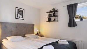A hotel room with a bed, a headboard, a shelf with plants, a window with curtains, and a framed picture on the wall. - 5 Star Holiday Home in Uddevalla (Uddevalla)