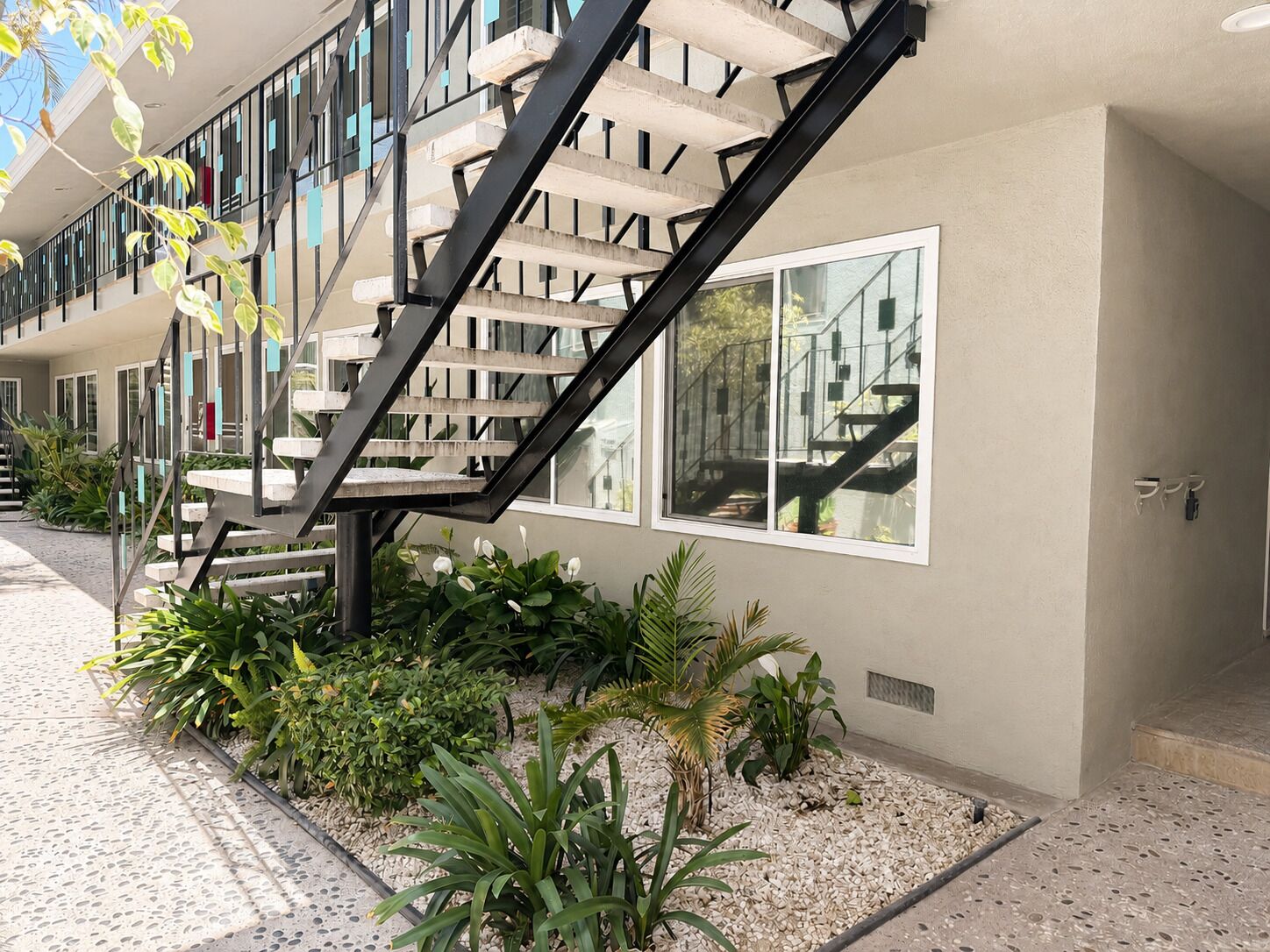 A modern building with a staircase, large windows, and a garden area with various plants.
