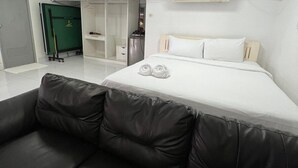 A room with a bed, a black leather sofa, a wardrobe, and a green door.