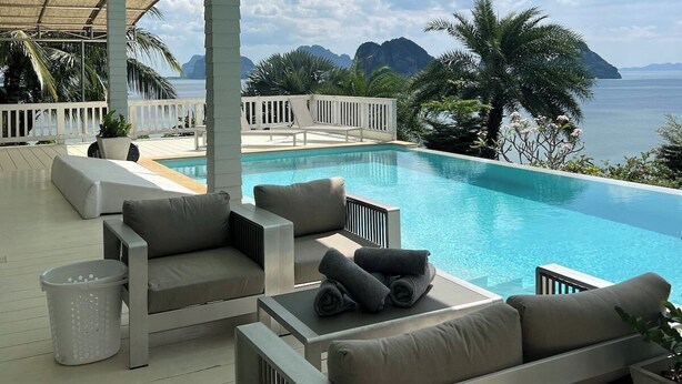 A poolside area with outdoor seating, a pool, and a view of the sea and mountains.