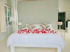 Une chambre à coucher avec un grand lit, du linge de lit blanc et une composition décorative de pétales de roses rouges.