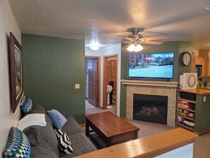 A living room with a sofa, coffee table, fireplace, television, and a ceiling fan. - The Royal Shreddar - Remote Work Ready (Frisco)