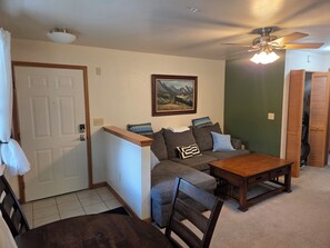 A living room with a sofa, a wooden coffee table, a ceiling fan, and a door. - The Royal Shreddar - Remote Work Ready (Frisco)