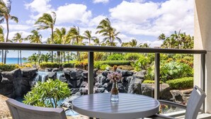 A balcony with a view of a tropical landscape, including palm trees and a waterfall.